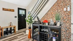 A modern interior with a staircase, a black door, a wooden bench, a console table with wine bottles, and a wall decorated with logs. - Bushkill Bliss w/ Hot tub near Falls & Shawnee (East Stroudsburg)