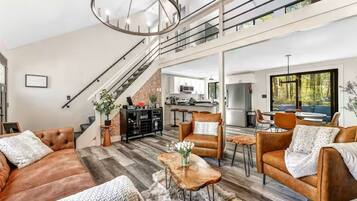 A spacious living area with a staircase, leather sofas, a wooden coffee table, and a kitchen in the background.