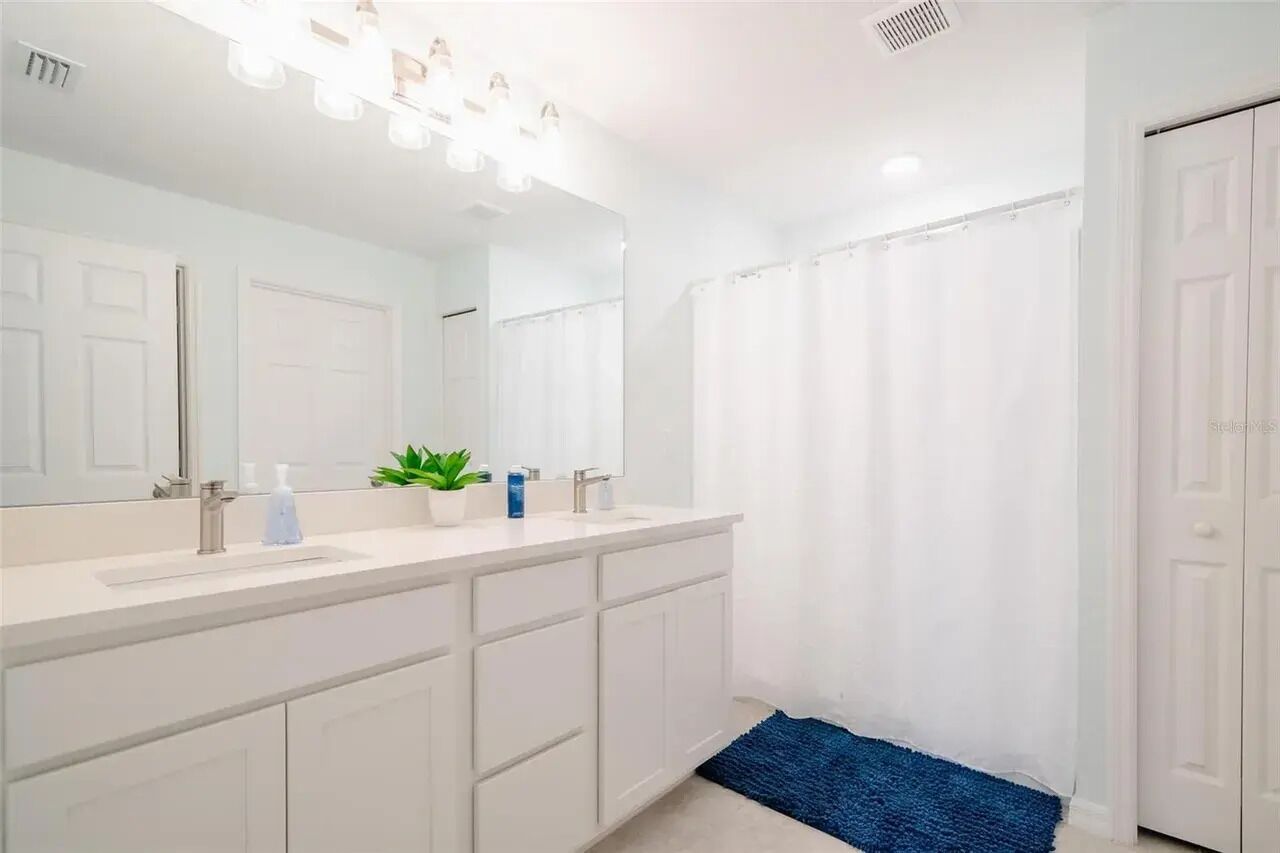 Une salle de bain avec un meuble-lavabo blanc, un grand miroir, un rideau de douche et un tapis bleu.