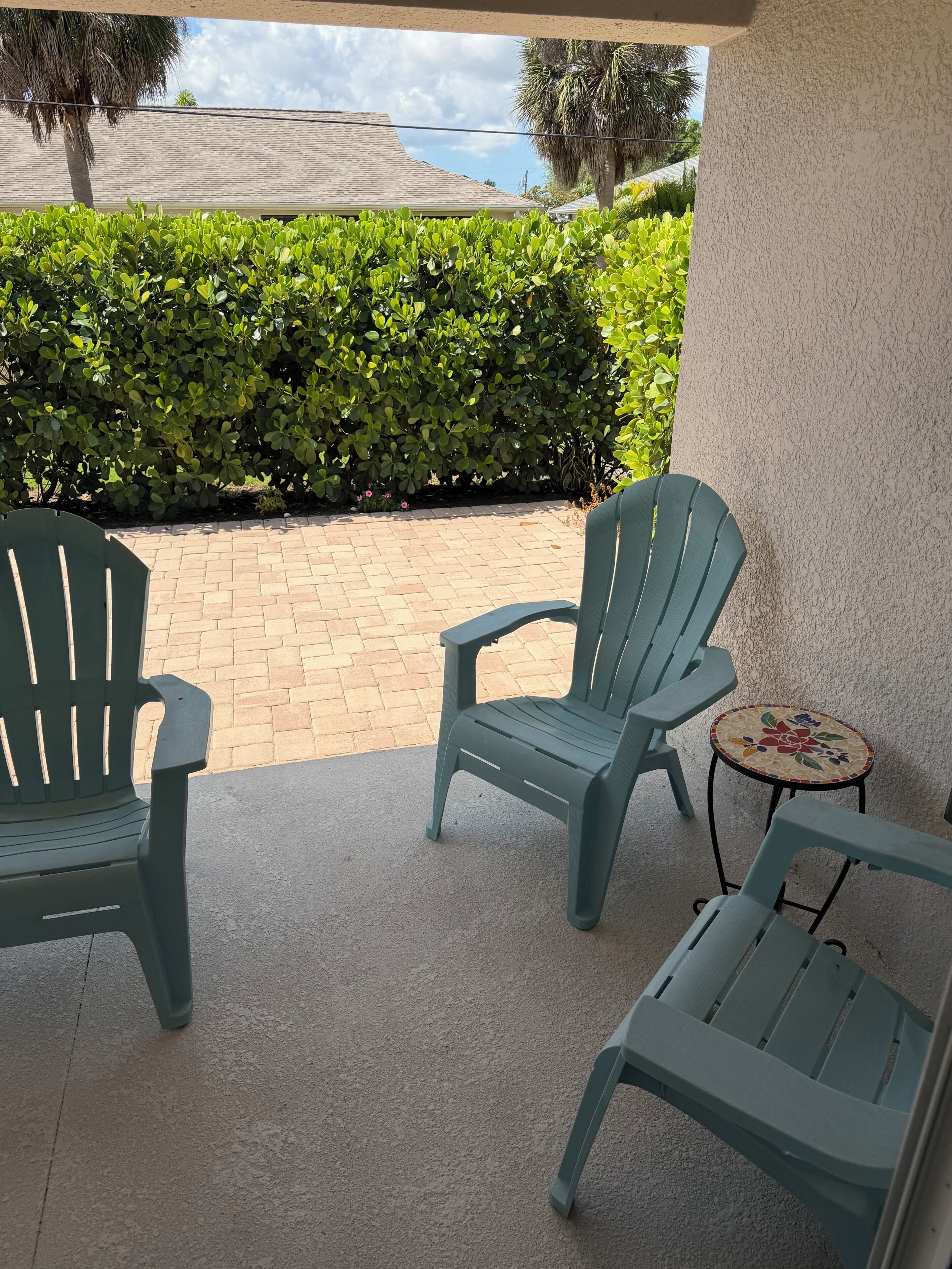Un patio cubierto con dos sillas Adirondack verdes y una pequeña mesa redonda con diseño floral.