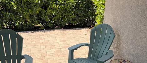 Un patio cubierto con dos sillas Adirondack verdes y una pequeña mesa redonda con diseño floral.