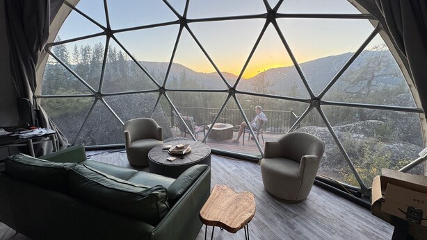 Una habitación tipo cúpula geométrica con vistas a las montañas, un sofá verde, dos sillones y una pequeña mesa de madera.