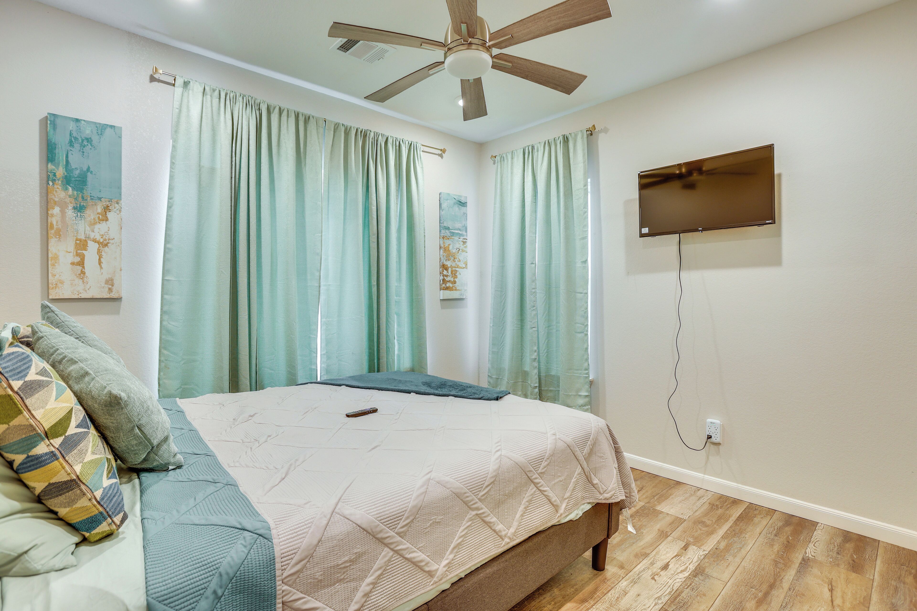 A bedroom with a bed, a ceiling fan, a TV mounted on the wall, and curtains.