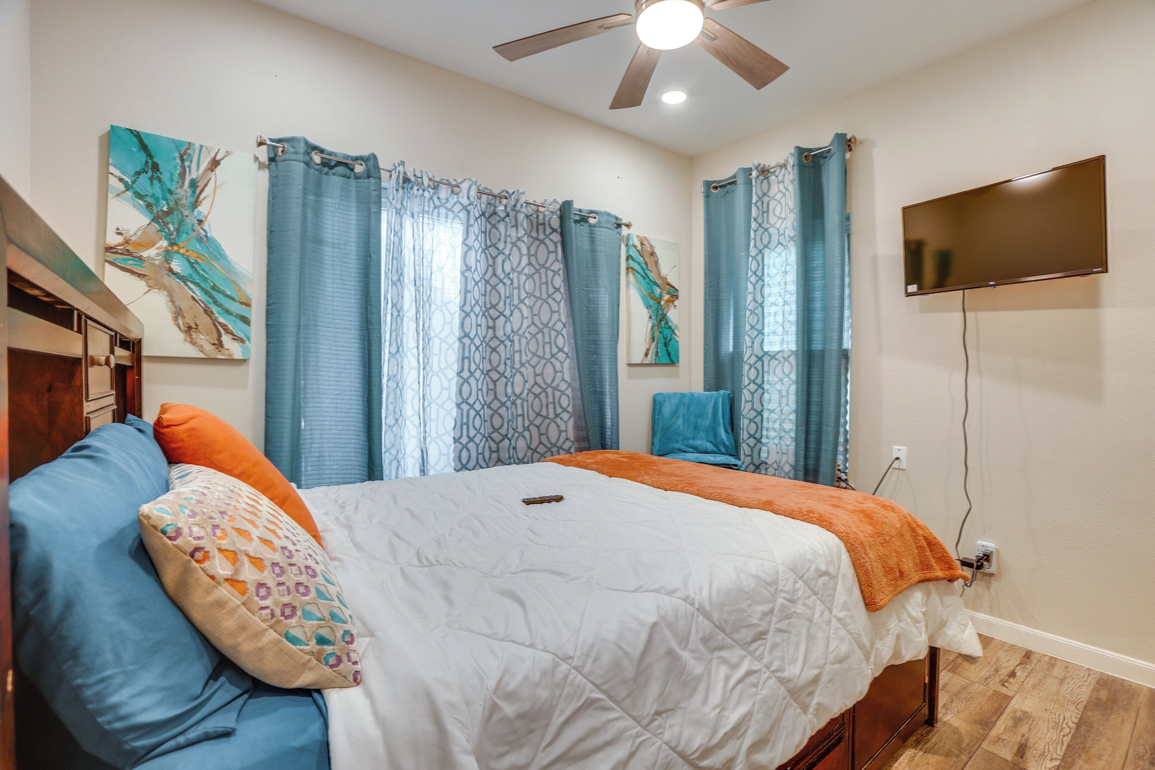 A bedroom with a bed, a ceiling fan, a TV, and artwork on the walls.