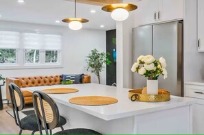 Una cocina moderna con armarios blancos, una isla central con un jarrón de flores e iluminación colgante.
