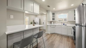 A modern kitchen with white cabinetry, a stainless steel refrigerator, and a bar area with two chairs. - Private Fort Worth Getaway Near Stockyards & Zoo! (Fort Worth)