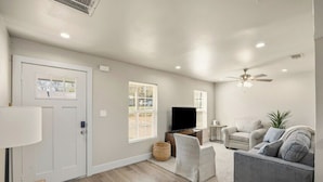 A living room with a grey sofa, a television, a ceiling fan, and a door with windows. - Private Fort Worth Getaway Near Stockyards & Zoo! (Fort Worth)