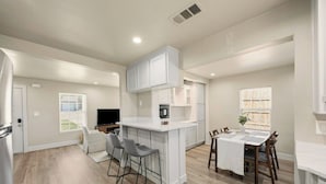 A modern kitchen with white cabinetry, a central island, bar stools, and a dining table with chairs. - Private Fort Worth Getaway Near Stockyards & Zoo! (Fort Worth)