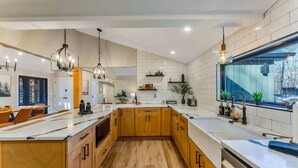 A modern kitchen with wooden cabinets, a large island, pendant lighting, and a view through a window. - Creek Retreat w/ Secluded 18-Acres, Hot Tub, Sauna (East Stroudsburg)