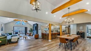 A spacious living area with a high ceiling, wooden beams, a dining table with chairs, and a kitchen in the background. - Creek Retreat w/ Secluded 18-Acres, Hot Tub, Sauna (East Stroudsburg)