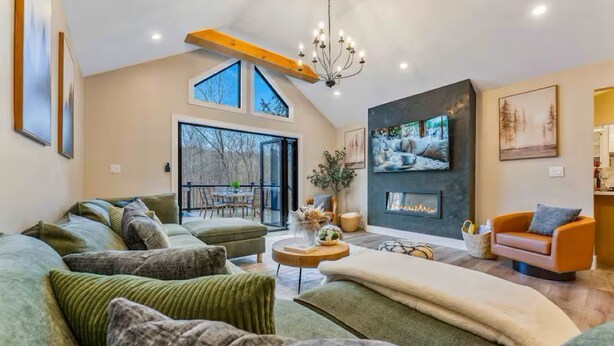 A spacious living room with a large sofa, a fireplace, and a dining area with natural light from large windows. - Creek Retreat w/ Secluded 18-Acres, Hot Tub, Sauna (East Stroudsburg)
