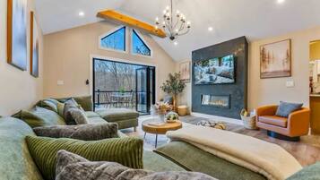 A spacious living room with a large sofa, a fireplace, and a dining area with natural light from large windows.