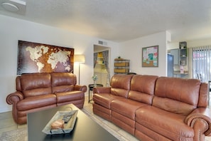 A living room with two brown leather sofas, a coffee table, a world map painting, a bulletin board, and a kitchen area in the background. - 3 Mi to Uptown Abq! Pet-friendly Condo w/ Patio (Albuquerque)