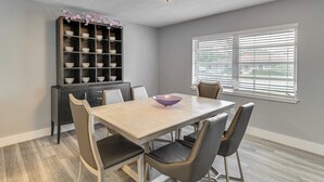 Un comedor con una mesa, sillas, un estante decorativo y una ventana con persianas.