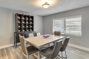 Un comedor con una mesa, sillas, un estante decorativo y una ventana con persianas.