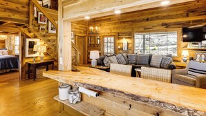 A log cabin interior with a wooden dining table, a sofa, and a staircase.