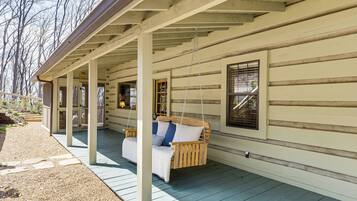 A covered porch with a swing chair, a wooden bench, and a small table.