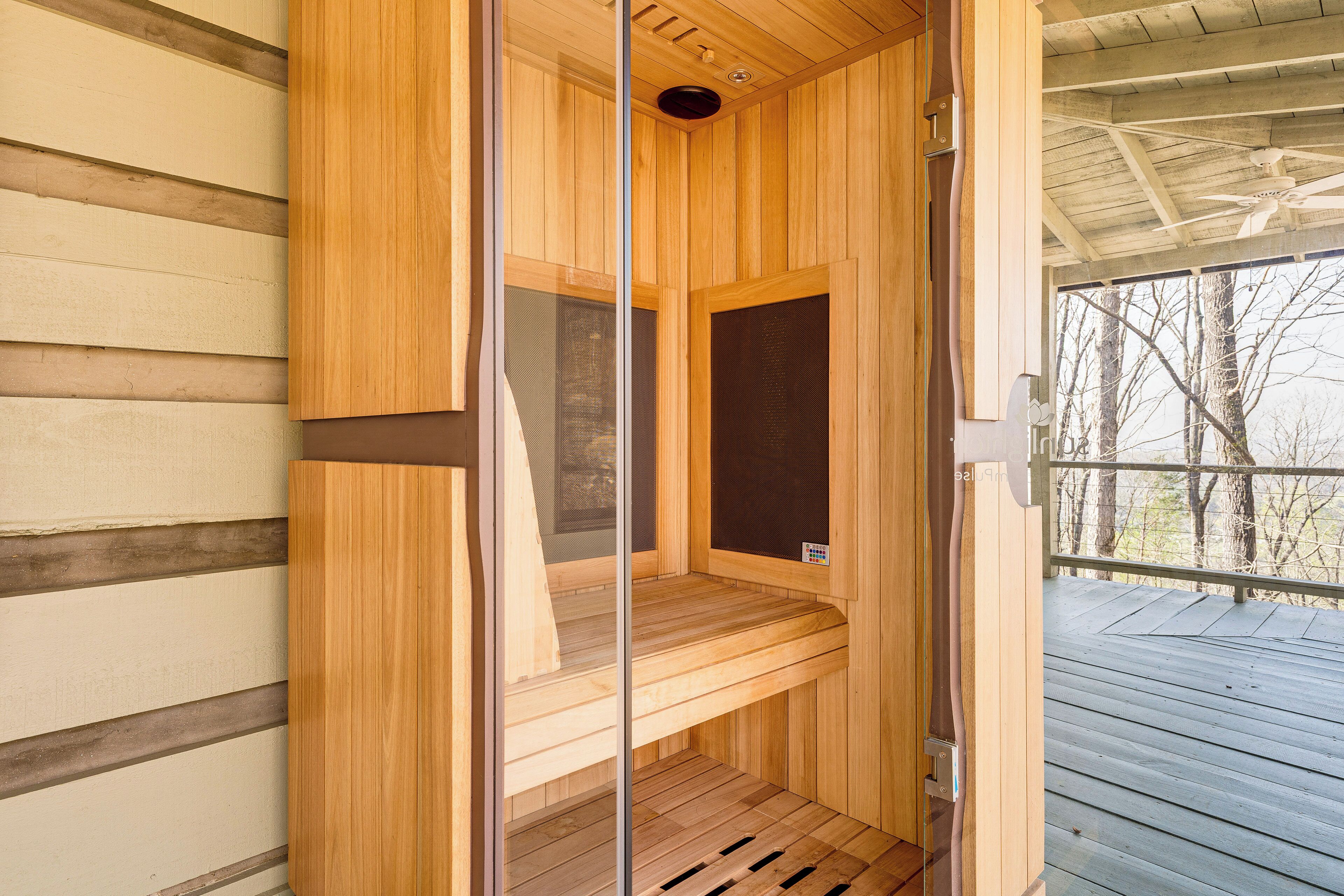 Eine Sauna mit Holzwänden und einer Bank, einem Deckenventilator und Blick auf Bäume.