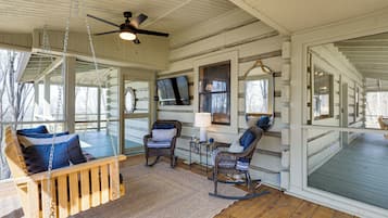 A wooden porch with rocking chairs, a swing, and a ceiling fan.