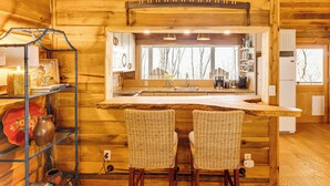 A wooden interior with a kitchen area, two wicker chairs, and a shelf with various items.