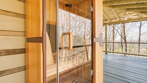 A sauna with a glass door, wooden interior, and a view of trees through the door.