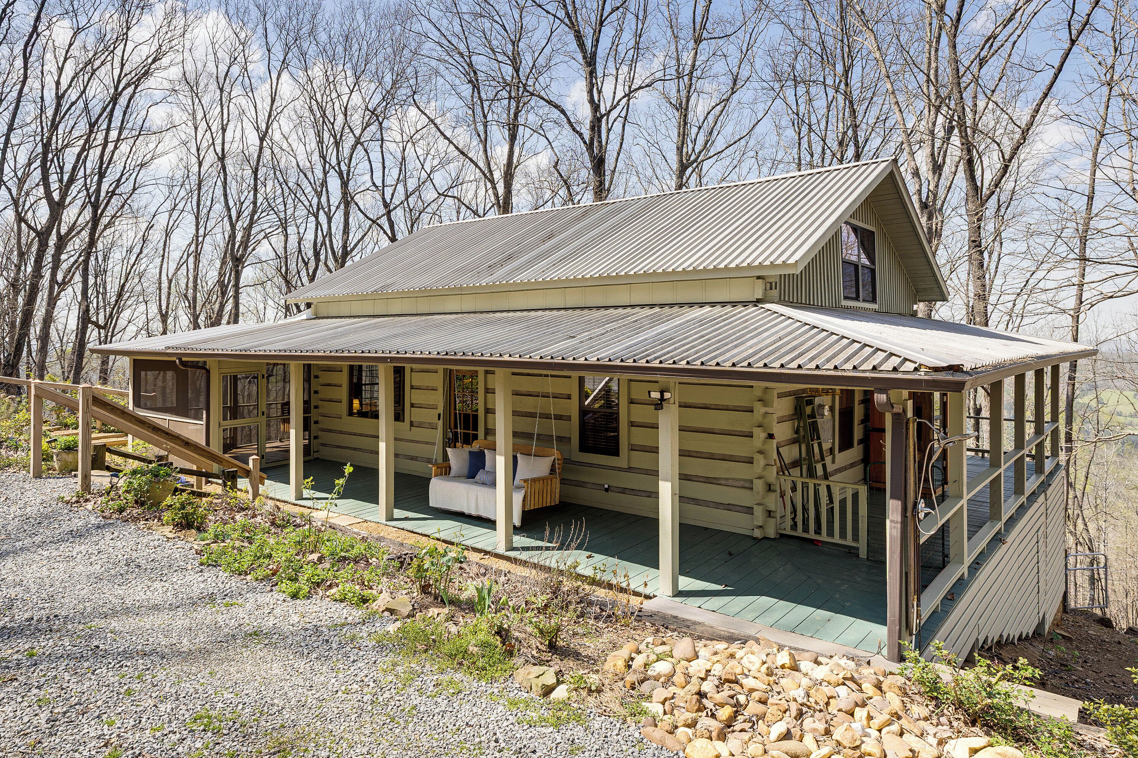 A log cabin with a porch, a swing, and a staircase leading to a deck.