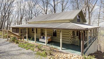 A log cabin with a porch, a swing, and a staircase leading to a deck.