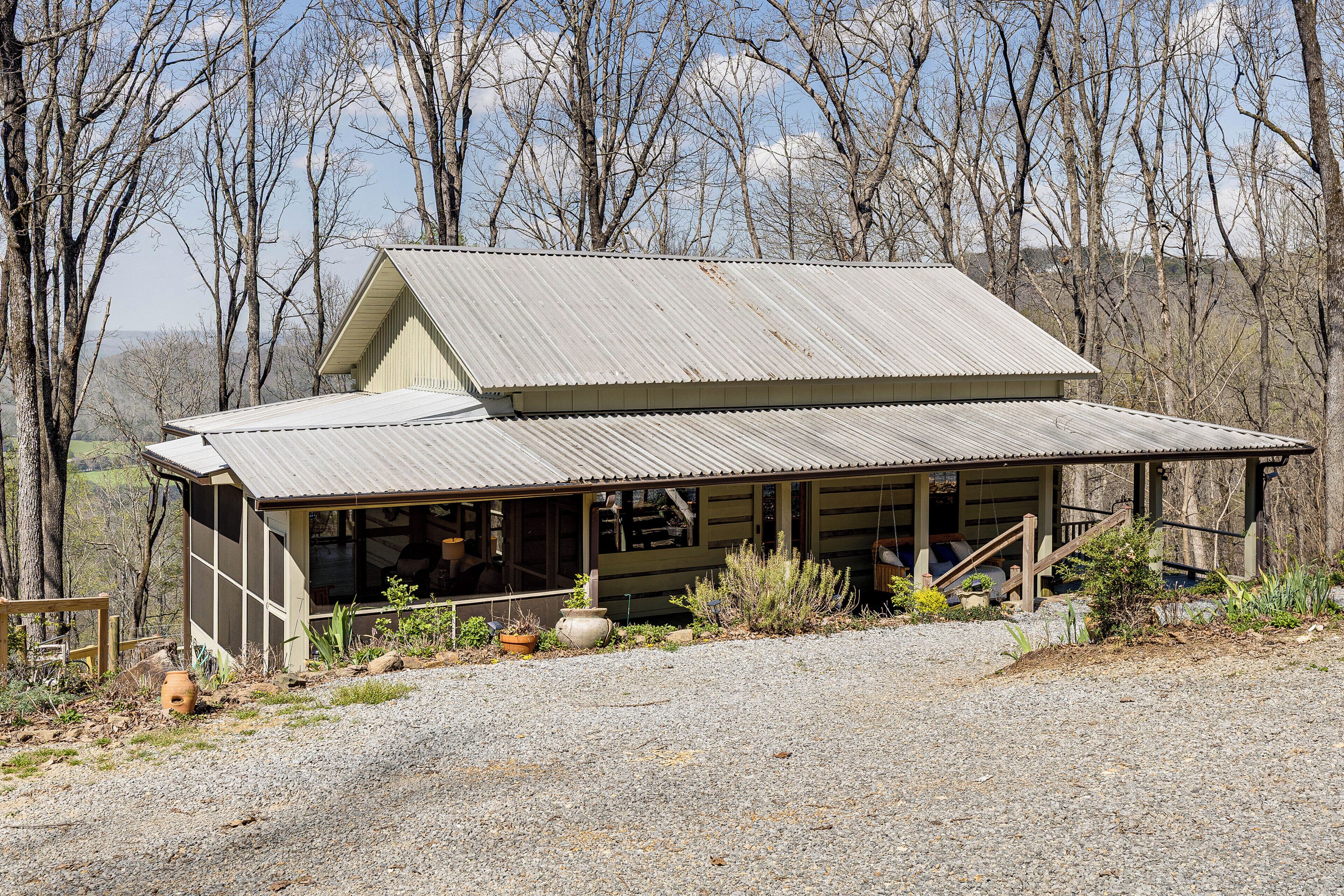 A rustic cabin with a metal roof, wooden porch, and a gravel driveway.
