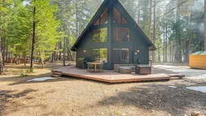 Eine Holzhütte mit Terrasse, Sitzgelegenheiten im Freien und Grillplatz, umgeben von einem Wald.