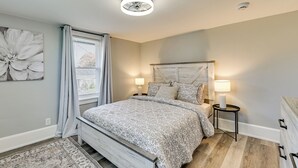 A bedroom with a bed, two bedside tables, a nightstand, a large window with curtains, and a wall-mounted artwork. - 4 Mi to Waterfront: 2-unit Combo in Kingston! (Kingston)