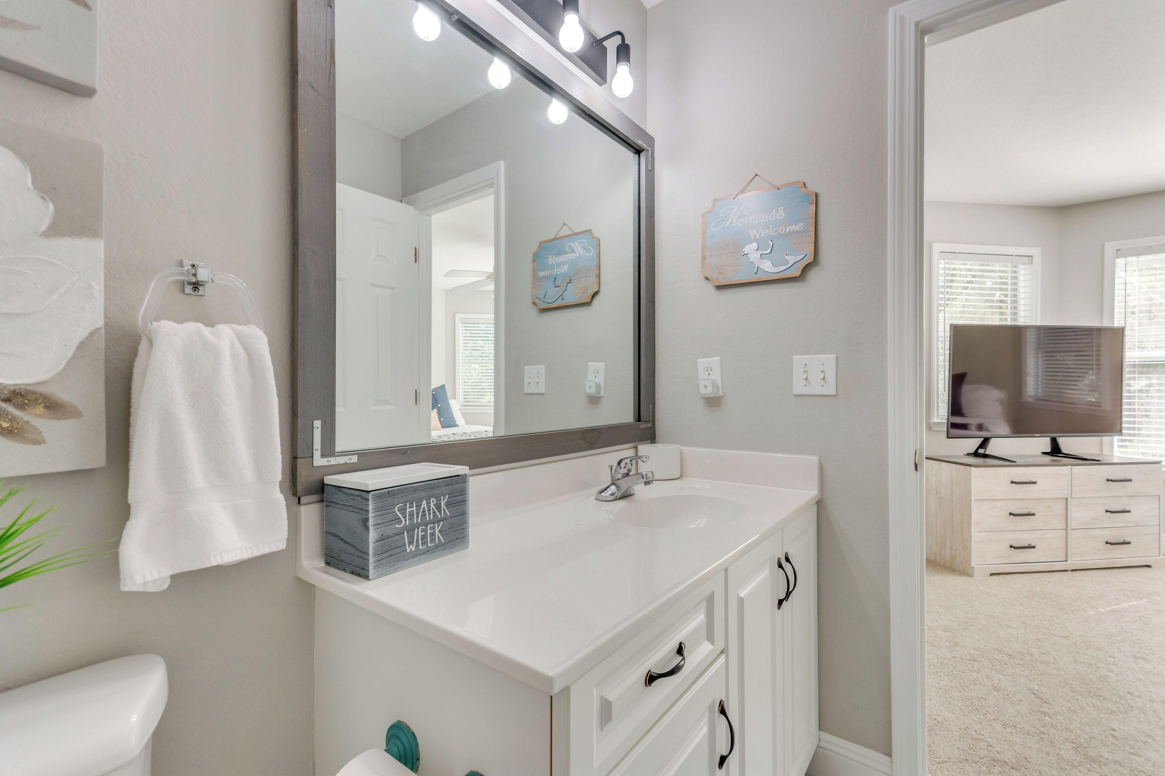 Un bagno con un mobile lavabo bianco, uno specchio grande e un cartello con scritto 'Shark Week'.