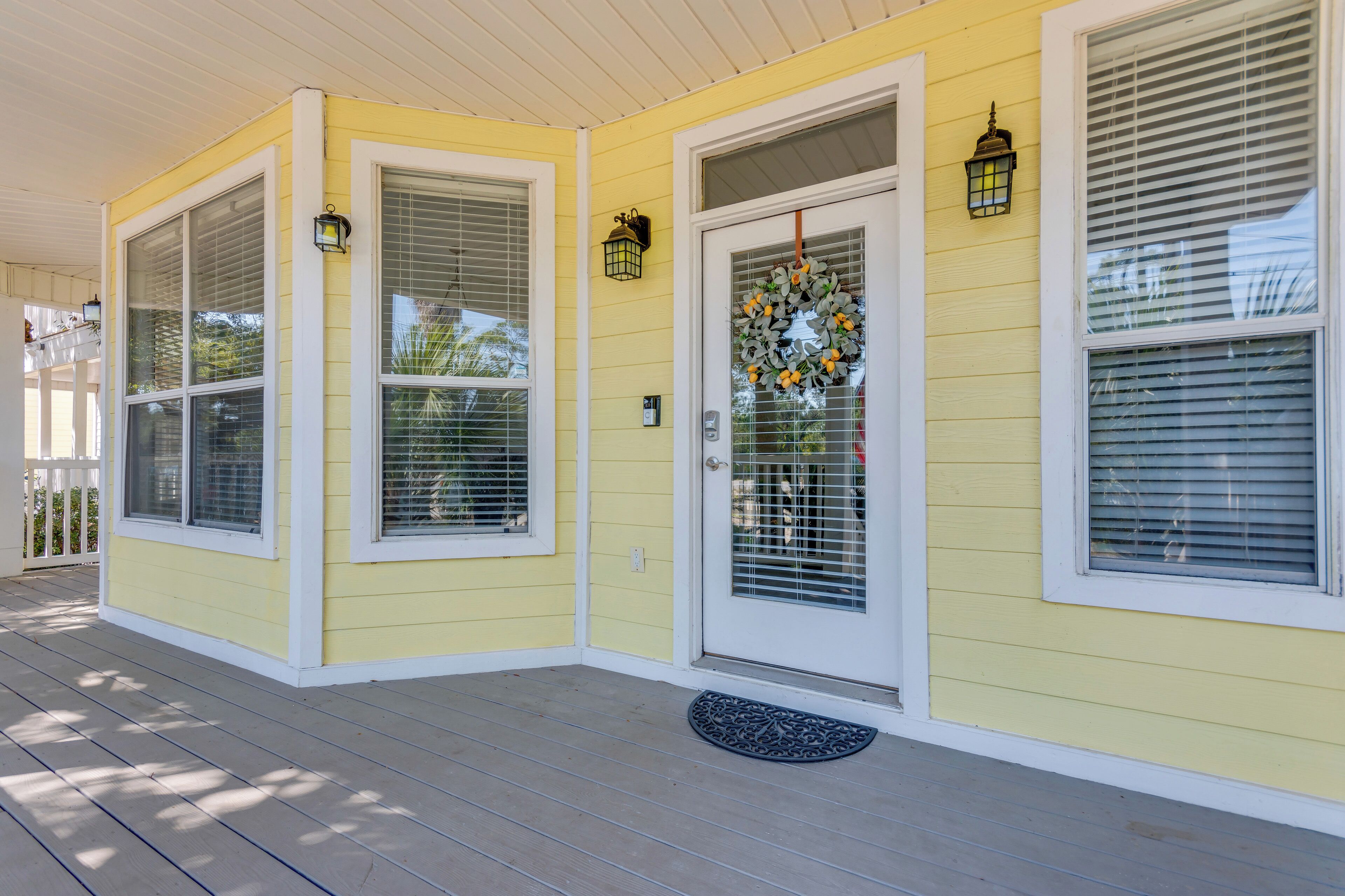 A yellow house with a porch, white trim, and a door with a wreath.
