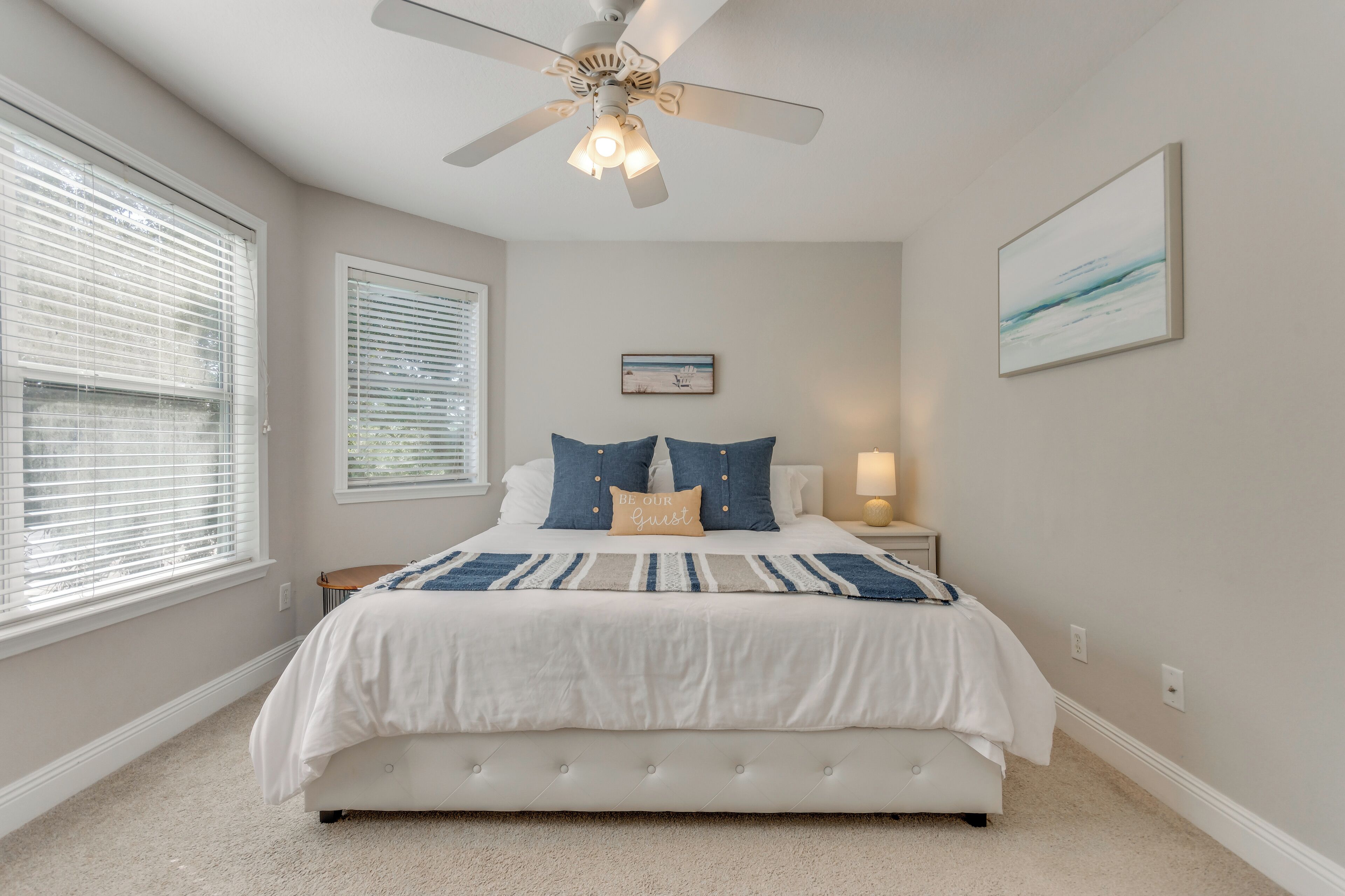 A bedroom with a bed, a ceiling fan, a nightstand, and a wall-mounted picture.
