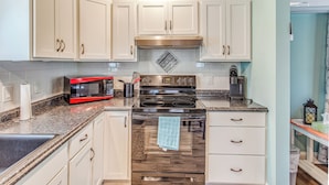 A kitchen with white cabinets, a stainless steel range hood, a black stove, and a microwave. - Bolivia Basecamp w/ Patio: 10 Mi to Oak Island (Bolivia)