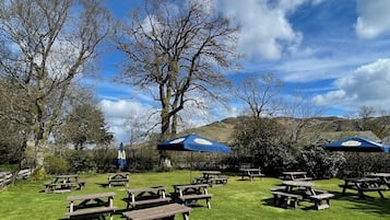 Un espacio al aire libre con mesas de picnic y sombrillas, rodeado de árboles y colinas.