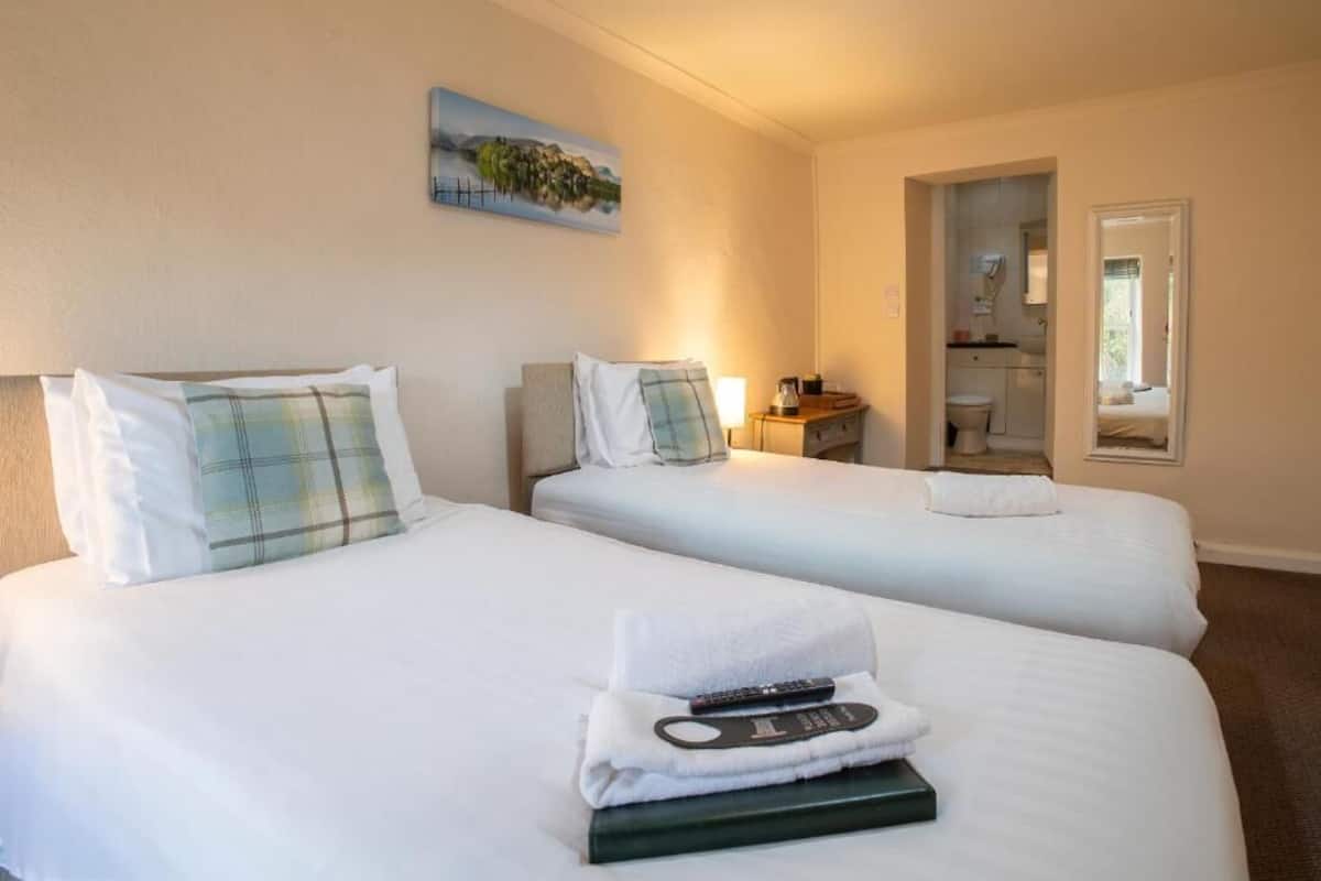 Habitación de hotel con dos camas, un cuadro en la pared, un baño visible a través de una puerta abierta y un control remoto sobre las camas.