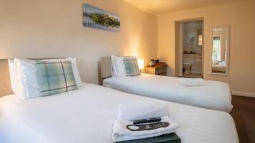 A hotel room with two beds, a painting on the wall, a bathroom visible through an open door, and a remote control on the beds.