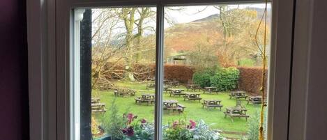 A window with a view of a garden with picnic tables.