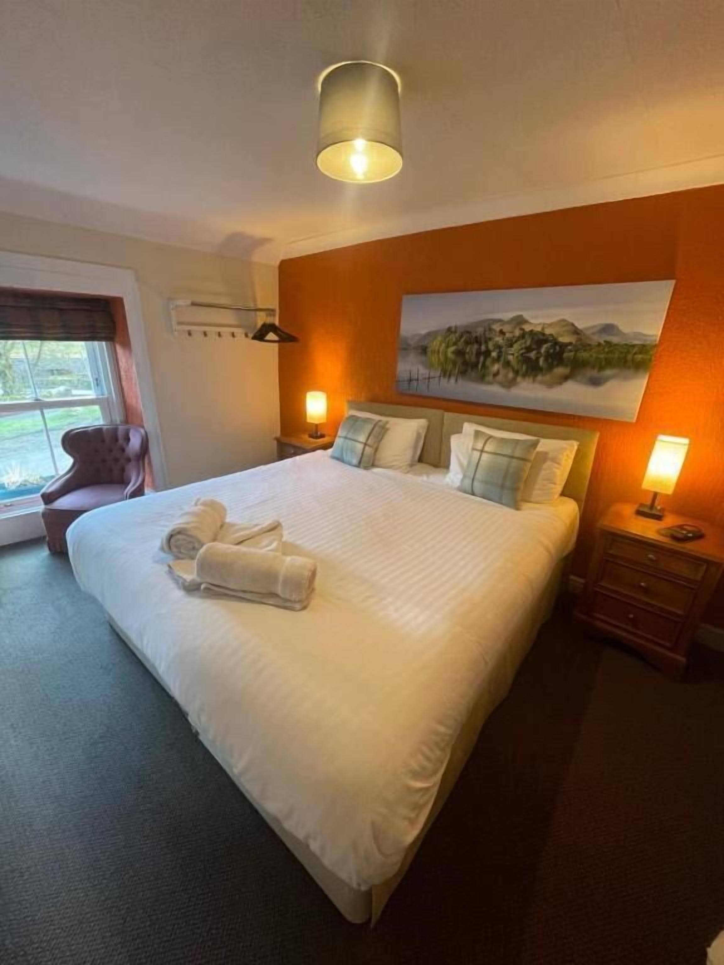 Una camera d'albergo con un letto grande, un quadro appeso al muro, una finestra con tende e una lampada da comodino.