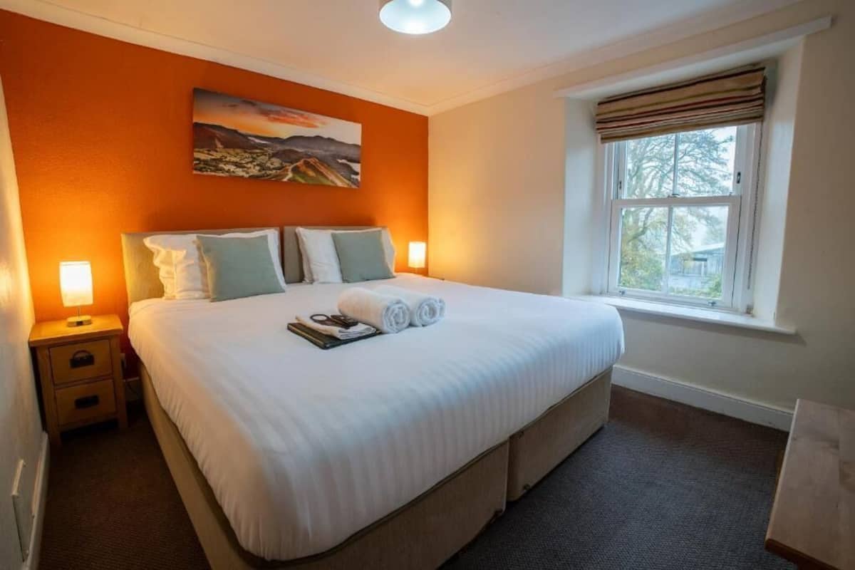 Una habitación de hotel con una cama grande, dos mesitas de noche, una ventana con cortinas y un cuadro en la pared.