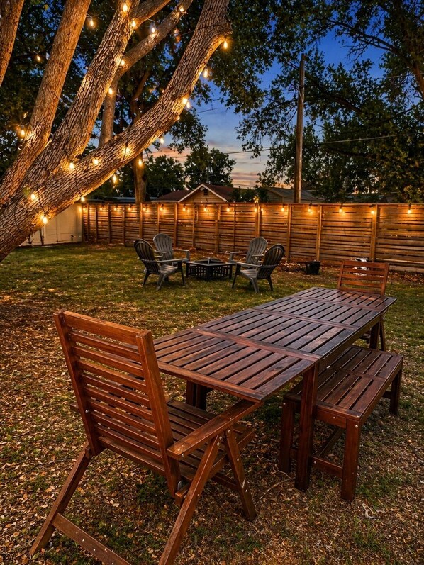 Une terrasse en bois avec une table et des chaises, entourée d’une clôture en bois et illuminée de guirlandes lumineuses.