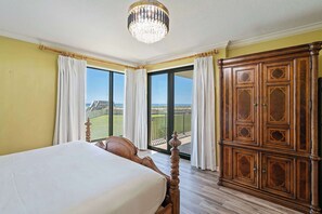 A bedroom with a bed, a wooden wardrobe, and a balcony with a view. - Navarre Towers 101 - 3 Bedroom (Navarre)
