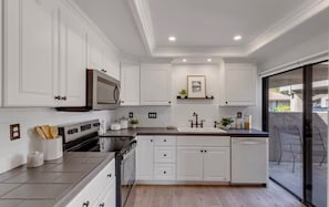A modern kitchen with white cabinetry, stainless steel appliances, and a large island. - Charming South Palm Desert Condo (Palm Desert)