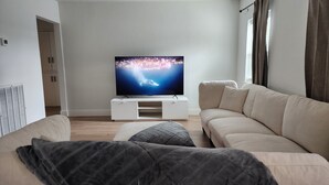 Een moderne woonkamer met een flatscreen televisie, een beige bank en een witte entertainmentkast.