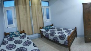 A bedroom with two single beds, a wooden wardrobe, a television mounted on the wall, and a small table with a patterned tablecloth. - Marsa allan star (Marsa Alam)