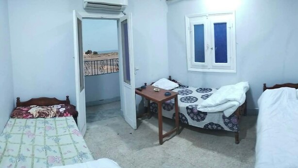 A small, compact room with a bed, a desk, a chair, a TV, and a window. - Marsa allan star (Marsa Alam)