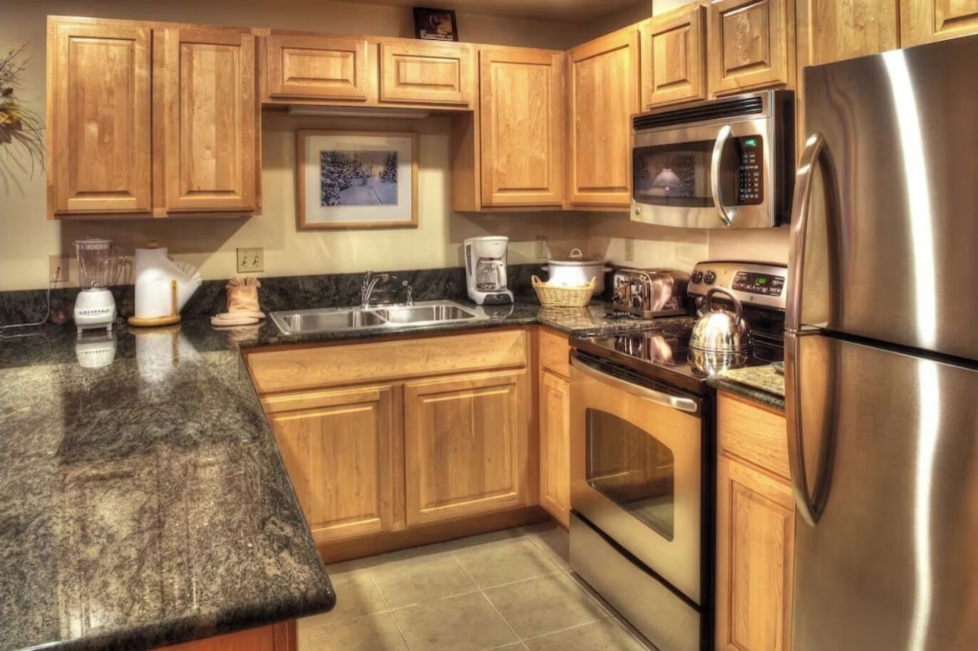 A kitchen with wooden cabinets, a stainless steel refrigerator, a microwave, a stove, and a sink.