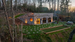 Een stenen huis met gebogen ramen en een stenen buitenkant, omgeven door een verzorgd gazon en bomen.