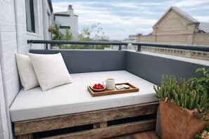 A balcony with a cushioned seating area, a tray with strawberries and a cup, and a potted plant. - Stylish 1BDR Redfern Retreat Walk to CBD Station (Redfern)