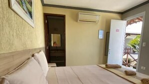 A hotel room with a bed, pillows, a painting on the wall, an air conditioning unit, and a door leading outside. - Pousada Pérola do Mar (Tamandaré)